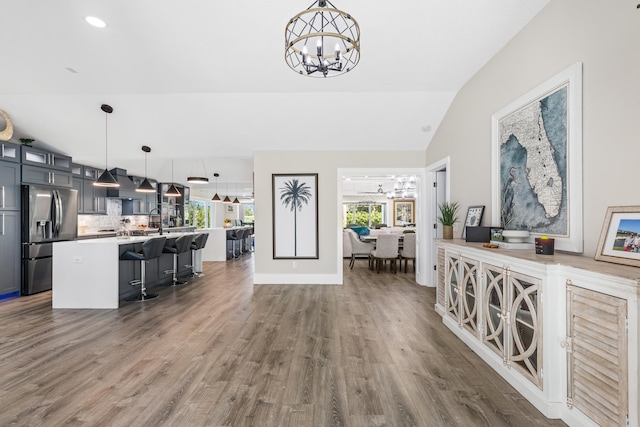 kitchen with a breakfast bar, stainless steel refrigerator with ice dispenser, an inviting chandelier, glass insert cabinets, and vaulted ceiling