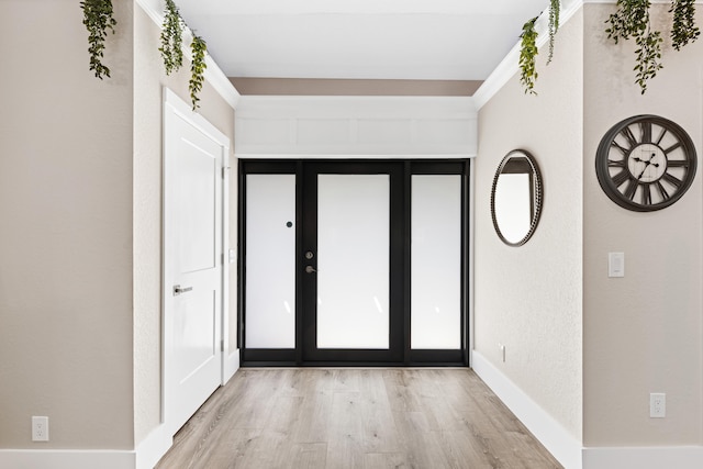 foyer featuring baseboards, light wood-style floors, and a textured wall