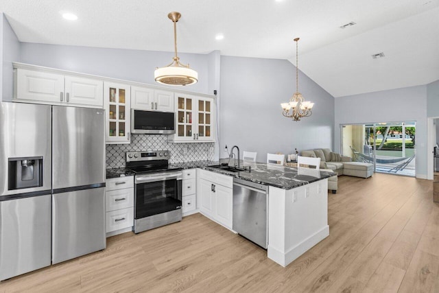 kitchen with a sink, stainless steel appliances, a peninsula, glass insert cabinets, and lofted ceiling