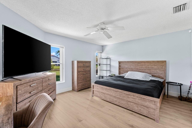 bedroom with a ceiling fan, baseboards, visible vents, light wood finished floors, and a textured ceiling