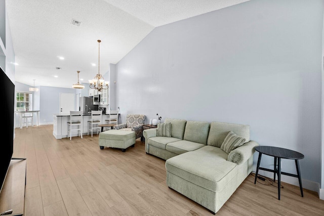 living room featuring visible vents, baseboards, light wood finished floors, vaulted ceiling, and a notable chandelier