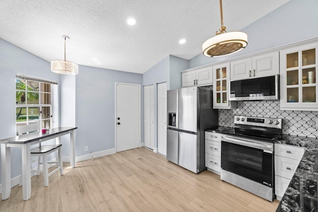 kitchen with light wood finished floors, vaulted ceiling, glass insert cabinets, appliances with stainless steel finishes, and backsplash