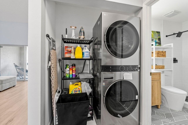 laundry area with laundry area, wood finished floors, visible vents, and stacked washer and clothes dryer