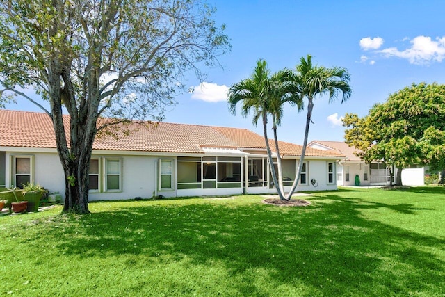 back of property featuring stucco siding, a lawn, a tiled roof, and a sunroom