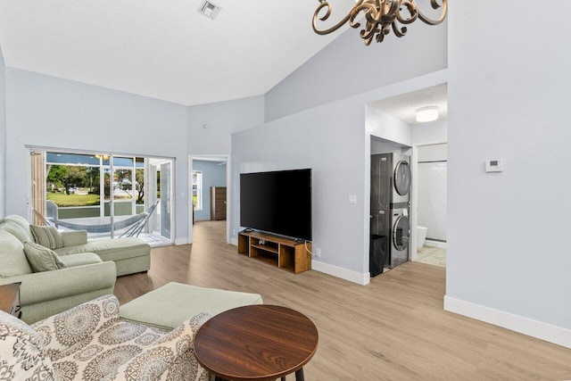 living room with visible vents, light wood-type flooring, an inviting chandelier, high vaulted ceiling, and stacked washer / drying machine