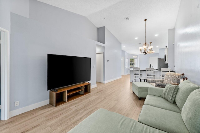 living room featuring visible vents, baseboards, a chandelier, lofted ceiling, and light wood-style flooring