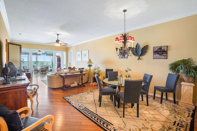 dining space with baseboards, ornamental molding, a textured ceiling, ceiling fan with notable chandelier, and light wood-type flooring