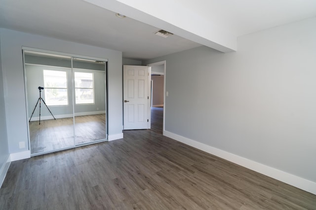 unfurnished bedroom with visible vents, baseboards, a closet, and dark wood finished floors