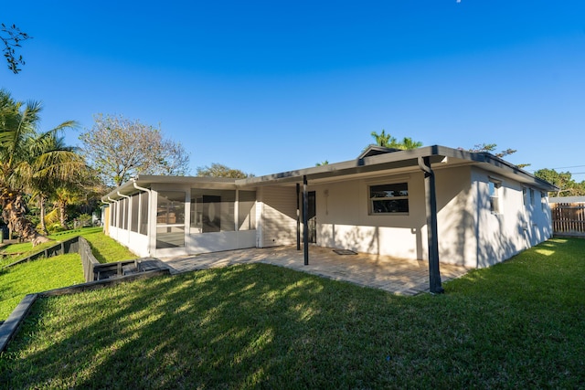 rear view of house featuring fence, stucco siding, a lawn, a sunroom, and a patio