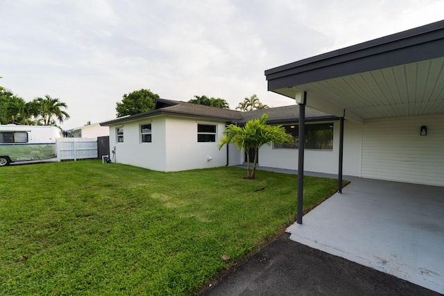 view of yard with an attached carport, concrete driveway, and fence