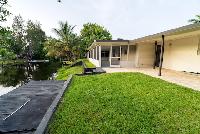 view of yard with a dock, a sunroom, and a water view