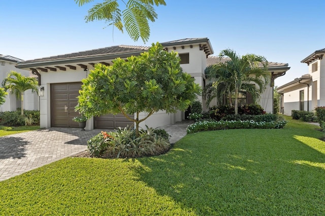 view of front of property featuring a front lawn, a tile roof, stucco siding, decorative driveway, and an attached garage