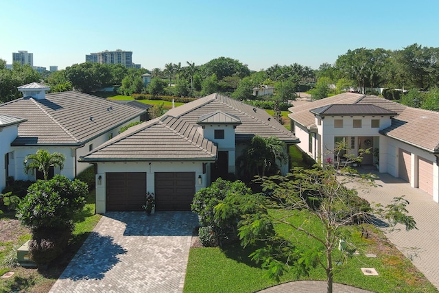 mediterranean / spanish-style house with an attached garage, a tiled roof, decorative driveway, and stucco siding
