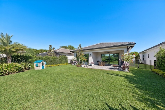 back of house featuring ceiling fan, fence, a shed, a lawn, and an outdoor structure