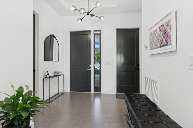 tiled foyer entrance featuring a raised ceiling, an inviting chandelier, and visible vents