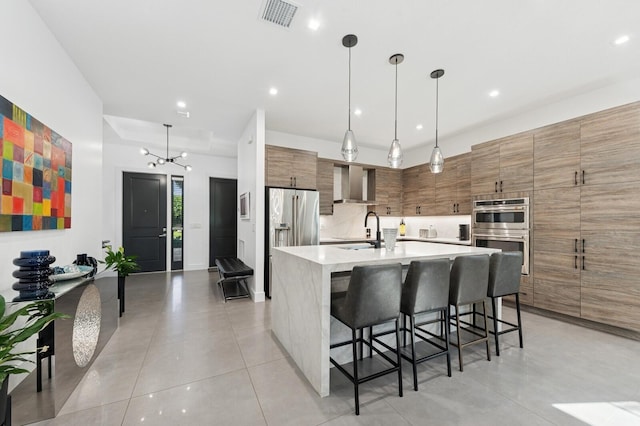 kitchen featuring brown cabinetry, modern cabinets, visible vents, wall chimney range hood, and appliances with stainless steel finishes