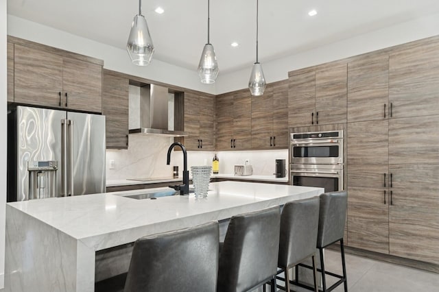 kitchen featuring wall chimney exhaust hood, a kitchen breakfast bar, modern cabinets, appliances with stainless steel finishes, and tasteful backsplash