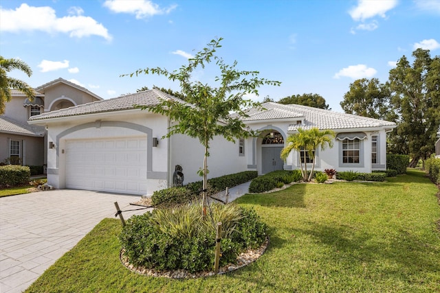 mediterranean / spanish home featuring a front yard, decorative driveway, stucco siding, a tiled roof, and an attached garage