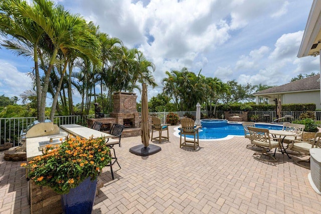 view of swimming pool with fence, exterior kitchen, a pool with connected hot tub, an outdoor stone fireplace, and a patio area