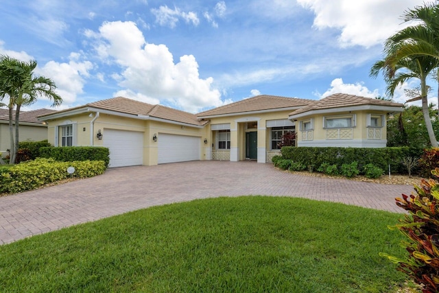 view of front of property featuring decorative driveway, a tile roof, an attached garage, and a front lawn