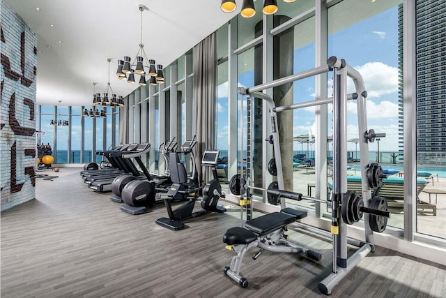 gym featuring wood finished floors, a chandelier, and expansive windows