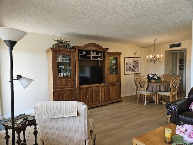 living area featuring baseboards, visible vents, light wood-style floors, a textured ceiling, and a notable chandelier