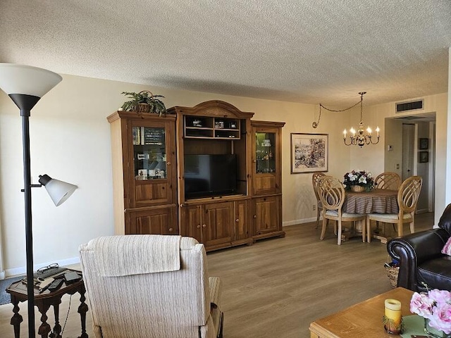 living area with baseboards, visible vents, a textured ceiling, a notable chandelier, and light wood-type flooring