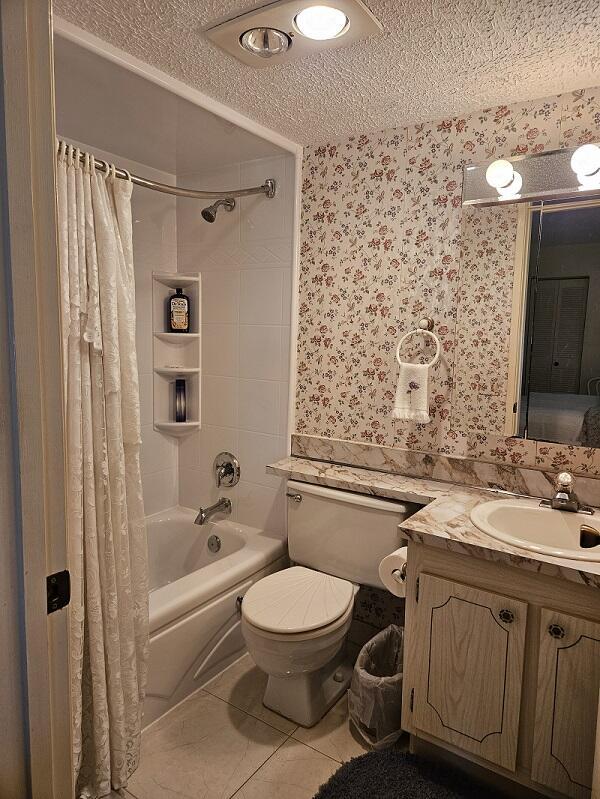 full bathroom with shower / bath combo with shower curtain, toilet, wallpapered walls, a textured ceiling, and tile patterned flooring