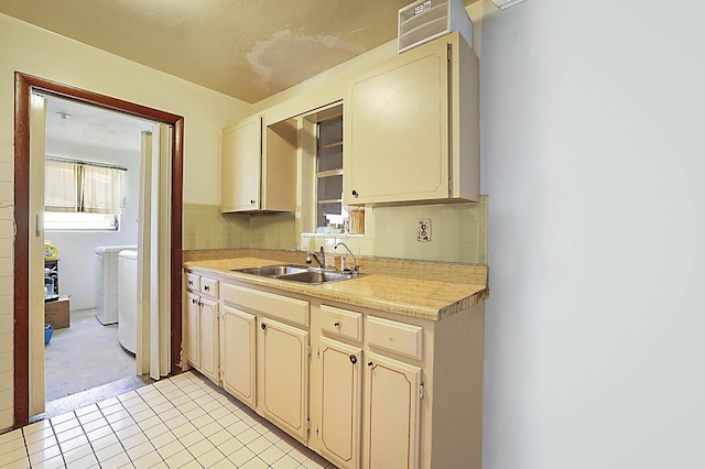 kitchen featuring tasteful backsplash, light countertops, cream cabinetry, washer and dryer, and a sink