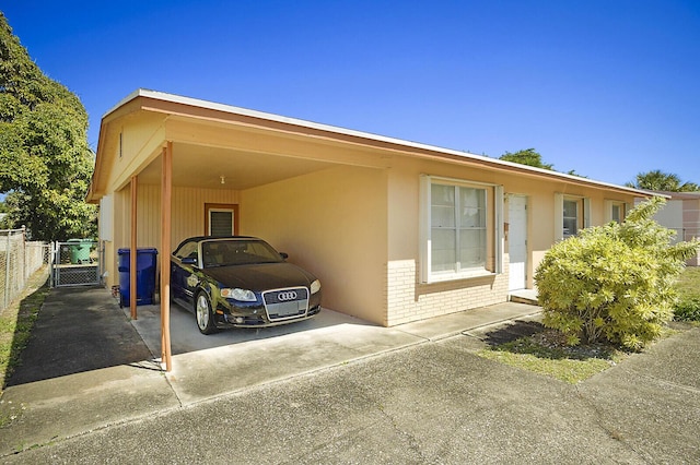 view of front facade featuring brick siding, concrete driveway, stucco siding, a carport, and a gate