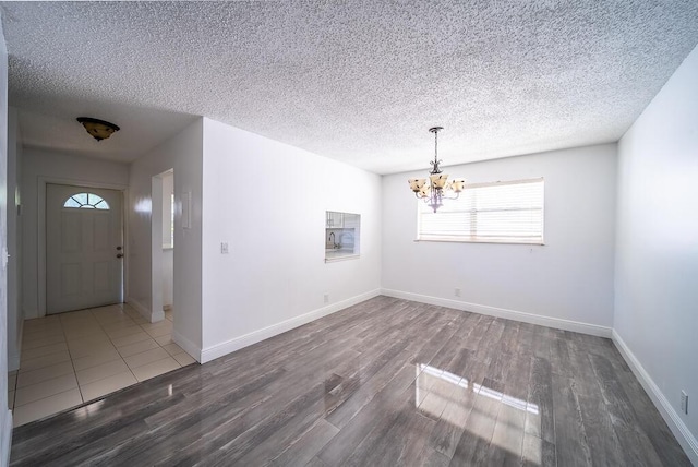 unfurnished dining area featuring a notable chandelier, wood finished floors, baseboards, and a textured ceiling