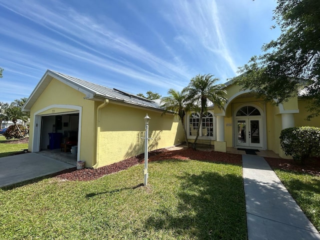 view of side of home featuring concrete driveway, stucco siding, french doors, a lawn, and metal roof