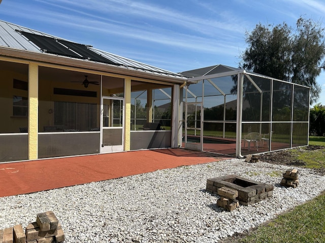 rear view of property featuring a fire pit, glass enclosure, metal roof, a patio area, and a standing seam roof