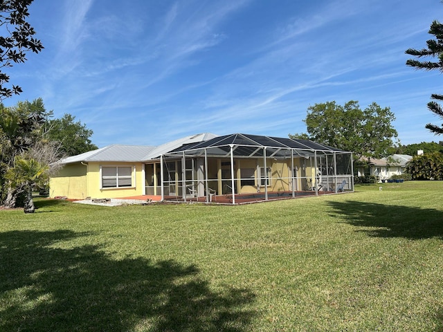 rear view of house featuring glass enclosure, a yard, and stucco siding