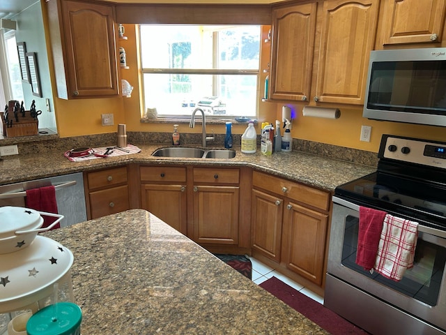 kitchen featuring a sink, stainless steel appliances, brown cabinetry, and dark stone counters