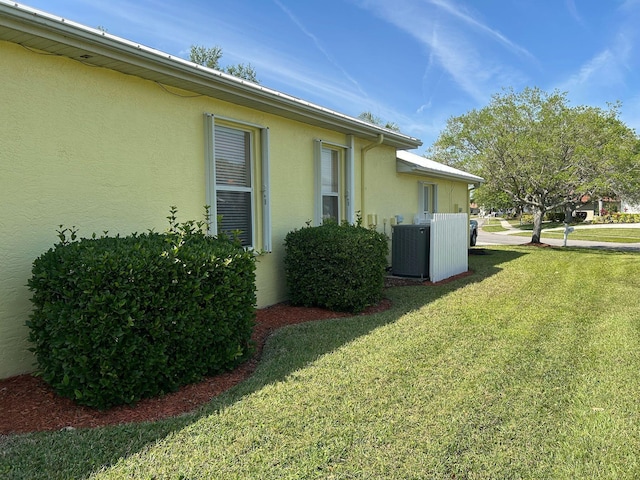 view of home's exterior with stucco siding, central AC, and a yard