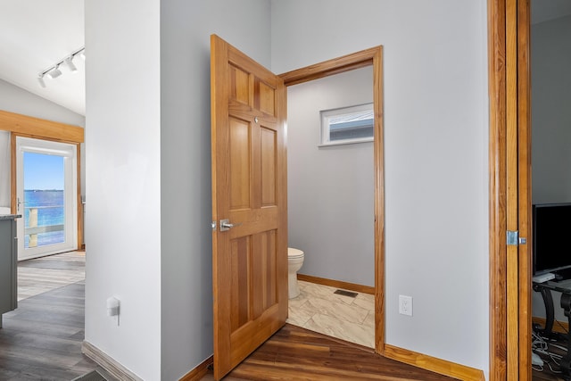 hall featuring track lighting, dark wood-style floors, baseboards, and visible vents