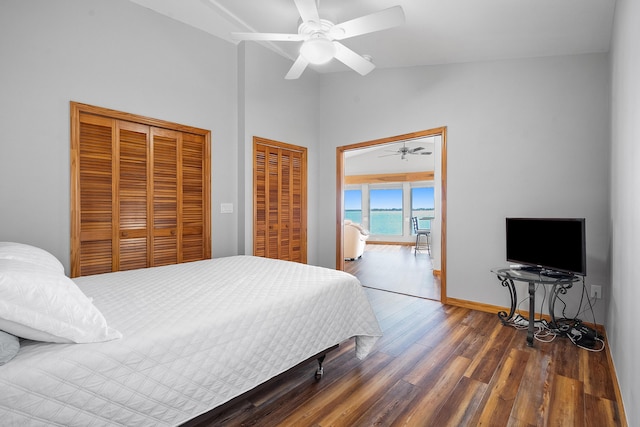 bedroom with two closets, baseboards, lofted ceiling, wood finished floors, and a ceiling fan