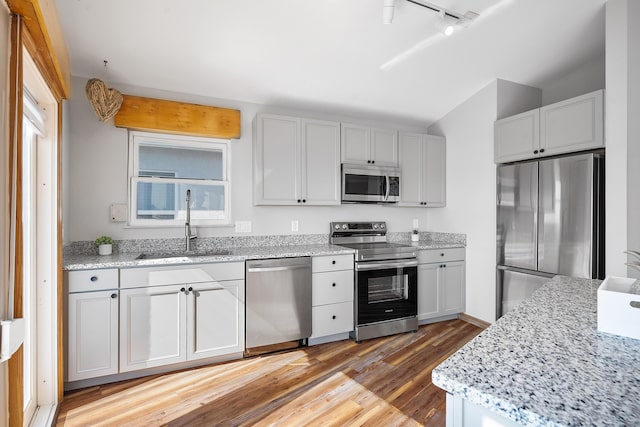 kitchen with light stone countertops, rail lighting, light wood-style floors, stainless steel appliances, and a sink