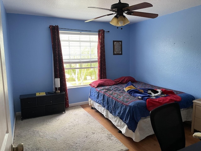 bedroom featuring a ceiling fan, wood finished floors, baseboards, and a textured ceiling