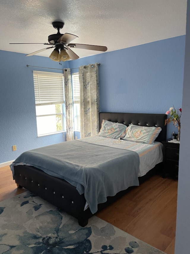 bedroom with ceiling fan, a textured ceiling, wood finished floors, and a textured wall