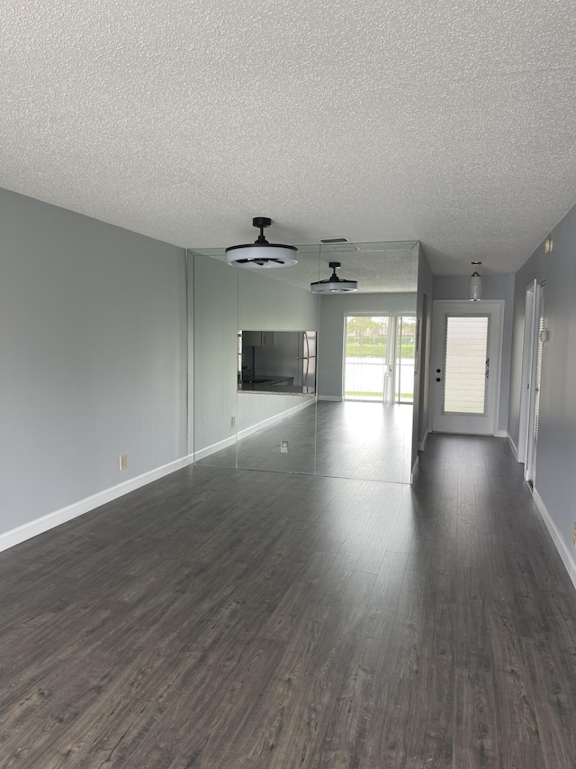 unfurnished living room with ceiling fan, baseboards, a textured ceiling, and dark wood-style floors