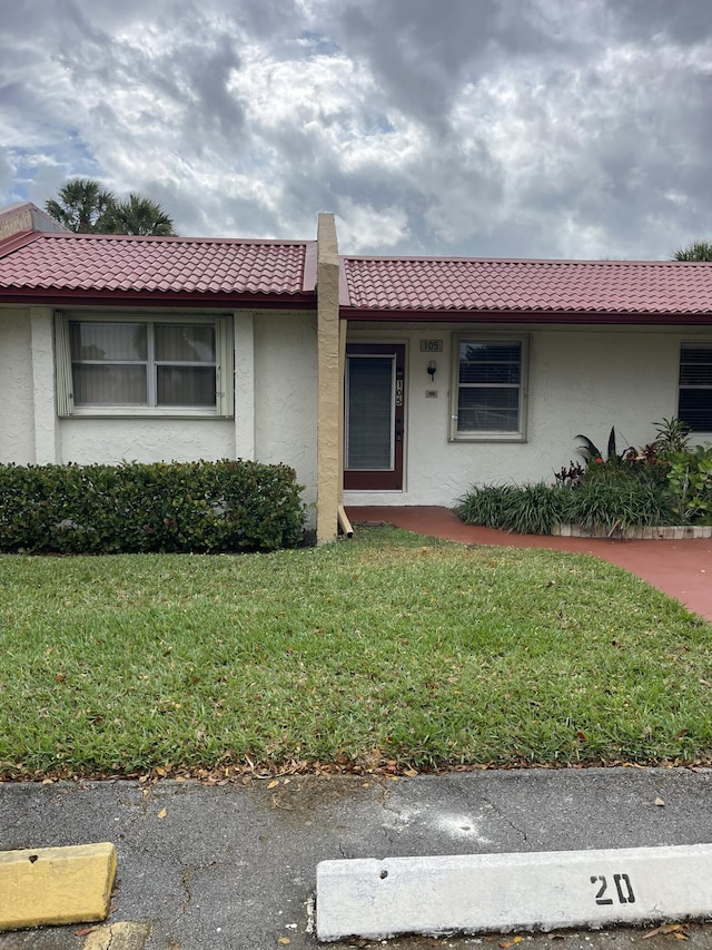 view of front facade featuring stucco siding, a front yard, and a tiled roof