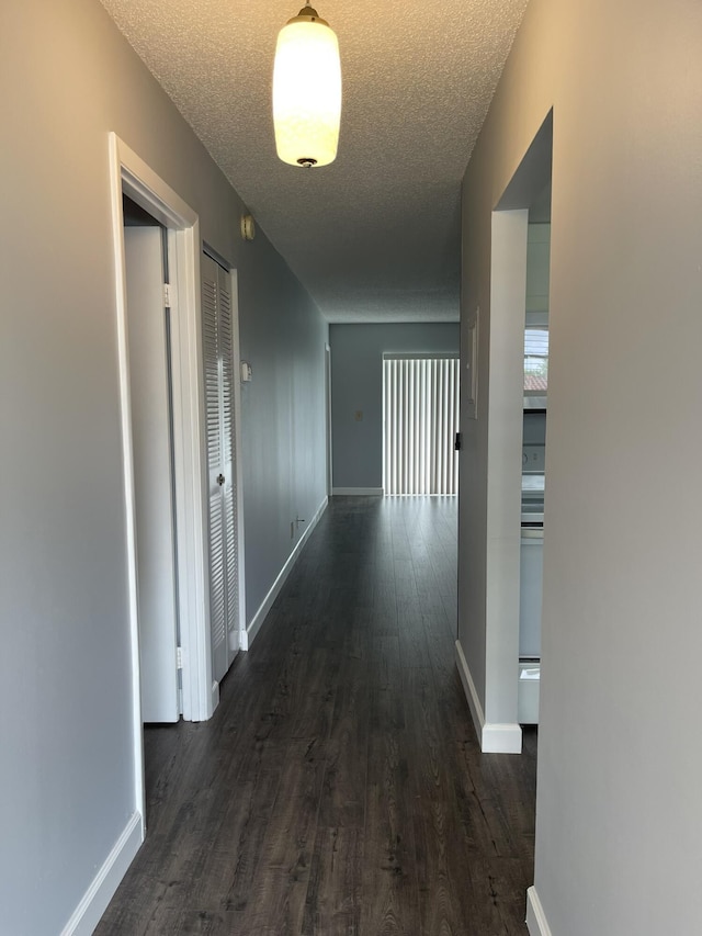 hall with baseboards, dark wood-type flooring, and a textured ceiling