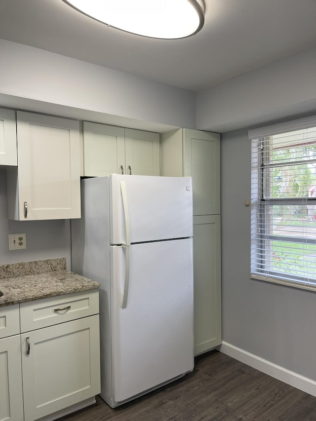 kitchen with light stone counters, baseboards, dark wood finished floors, freestanding refrigerator, and white cabinets
