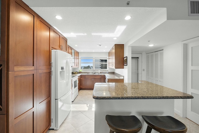 kitchen featuring visible vents, brown cabinets, a kitchen bar, a sink, and white appliances