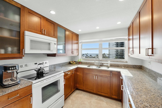 kitchen with a sink, white appliances, brown cabinetry, and light tile patterned floors