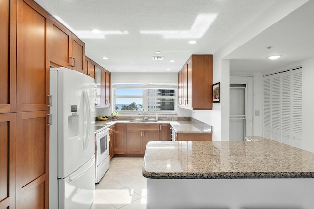 kitchen with white appliances, visible vents, stone counters, a sink, and brown cabinets