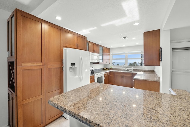 kitchen with white appliances, light stone counters, brown cabinetry, visible vents, and a sink