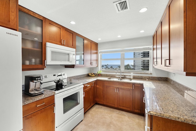 kitchen with white appliances, light stone counters, brown cabinetry, visible vents, and a sink